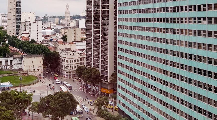 #PraCegoVer A foto mostra do lado direito, as fachadas de 2 prédios em destaque. No fundo, aparece a visão da rua, vista de cima.