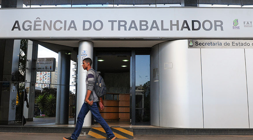 #PraCegoVer Jovem caminhando em frente a uma agência do trabalhador