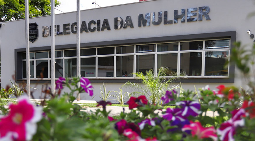 #PraCegoVer fachada da delegacia da mulher com flores do compo em primeiro plano um pouco desfocadas